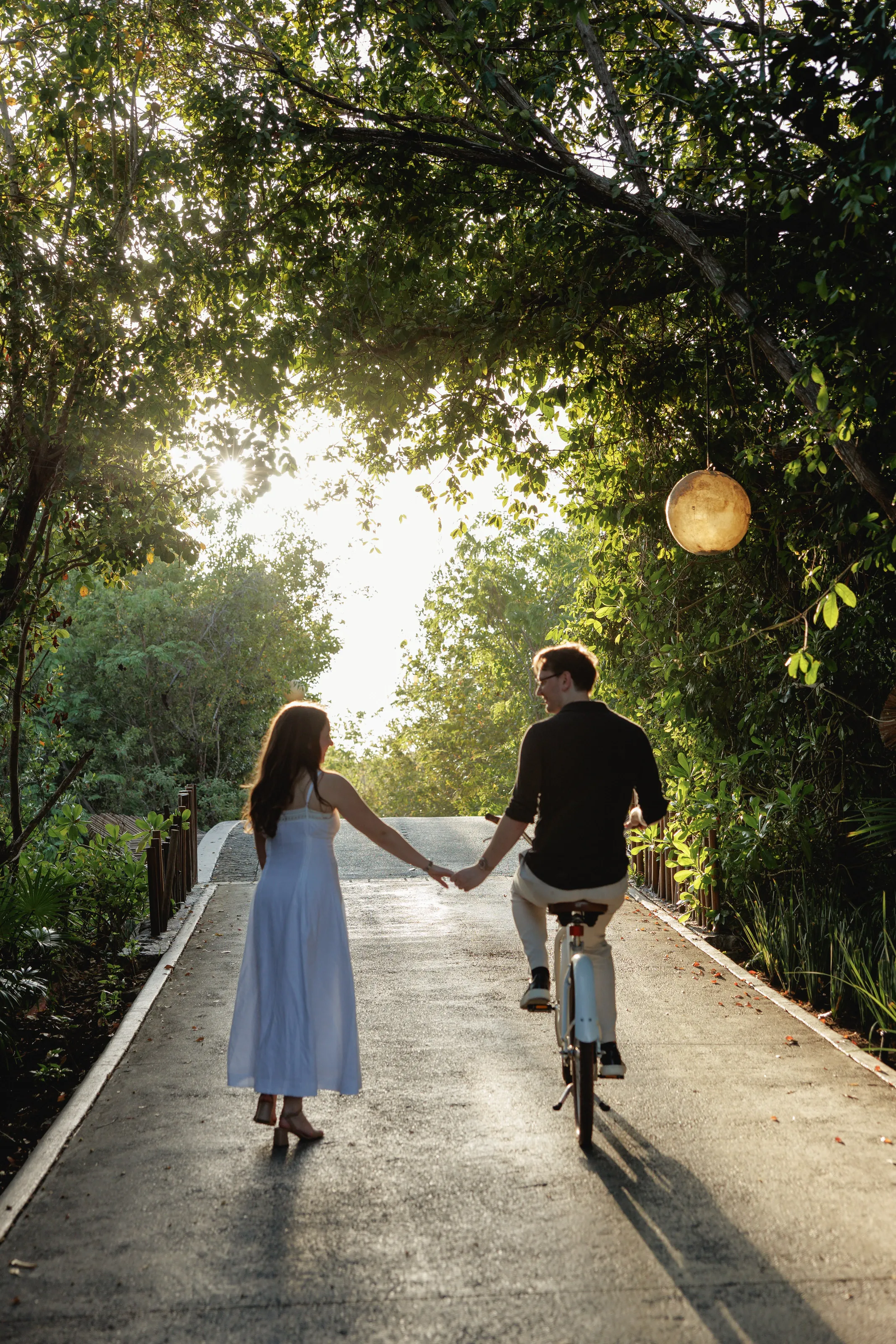 Ally and Marius holding hands on a tree-lined path at sunset